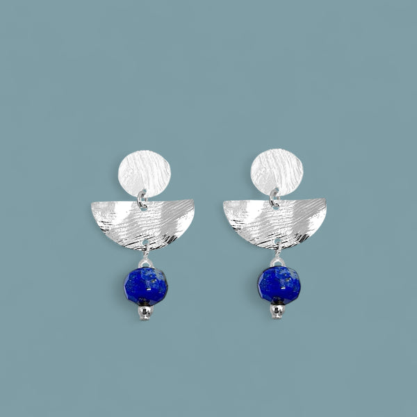 Boucles d'oreilles puces pendantes de forme demi-lune, en métal martelé argenté et perles de Lapis Lazuli, sur fond bleu gris