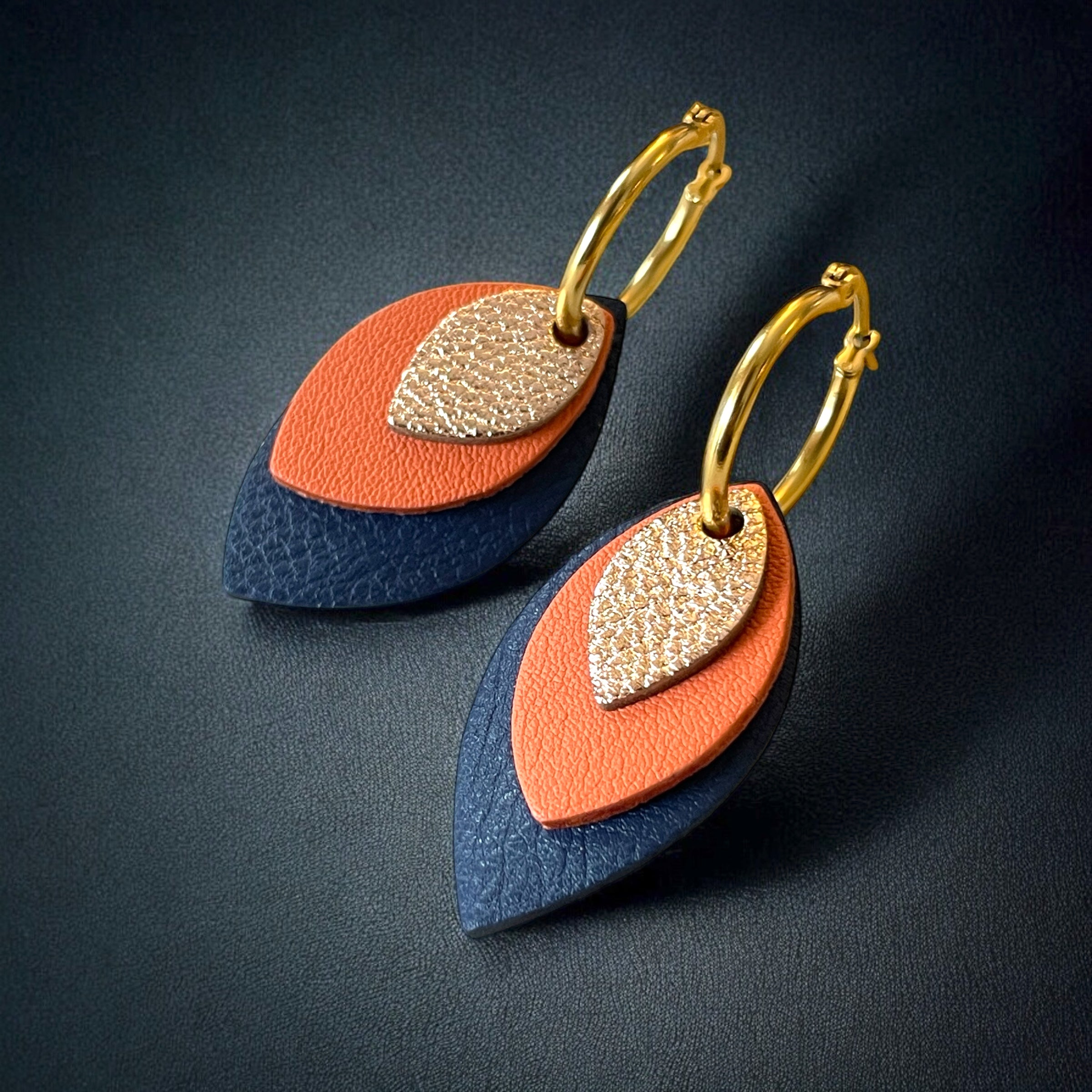Créoles dorées avec pendentifs modulables en forme de feuilles en cuirs rose pâle métallisé, saumon clair et bleu marine, sur fond noir