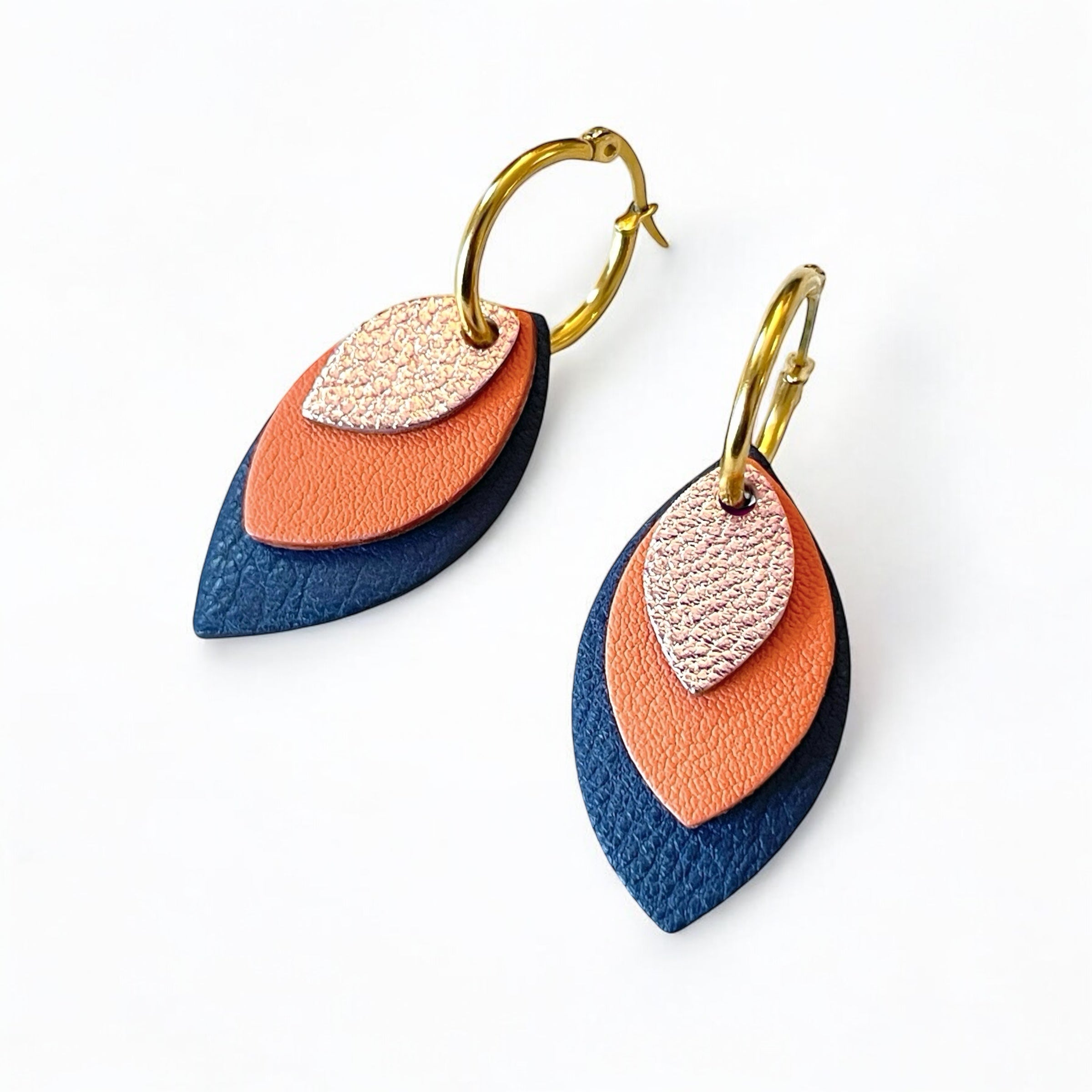 Créoles dorées avec pendentifs modulables en forme de feuilles en cuirs rose pâle métallisé, saumon clair et bleu marine, sur fond blanc