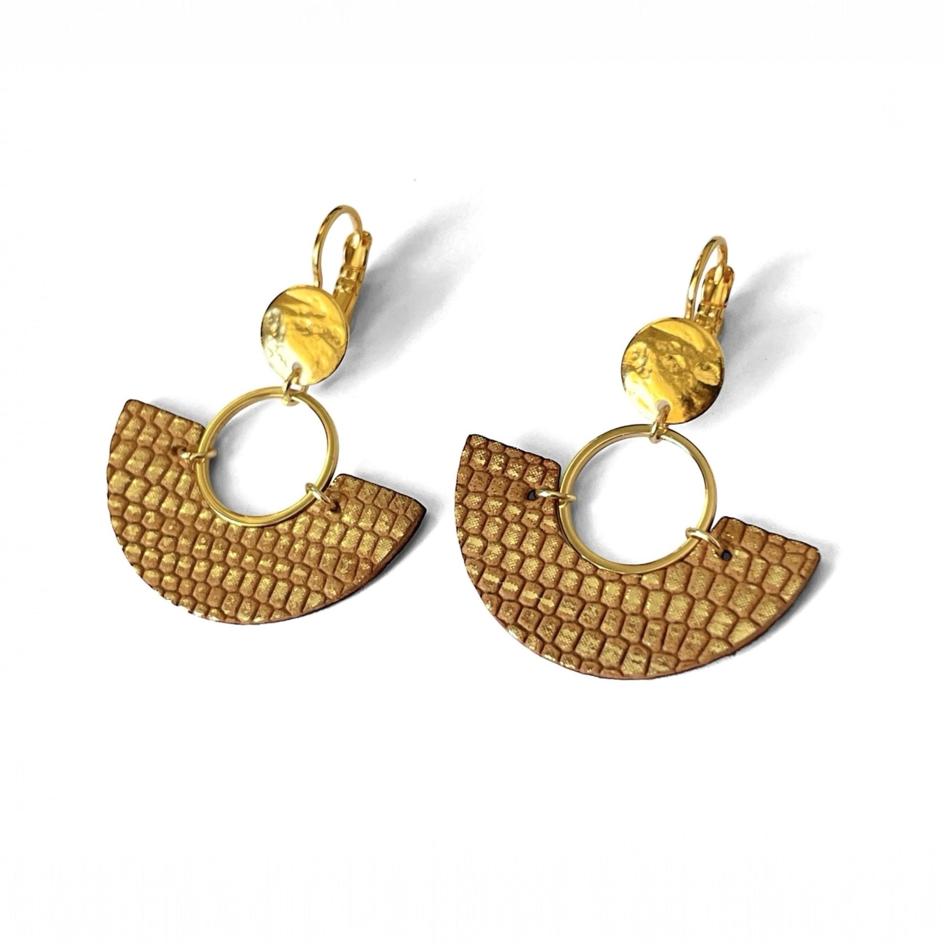 paire de boucles d'oreilles dorées pendantes en forme de demi-lunes en cuir sable doré façon serpent, sur fond blanc