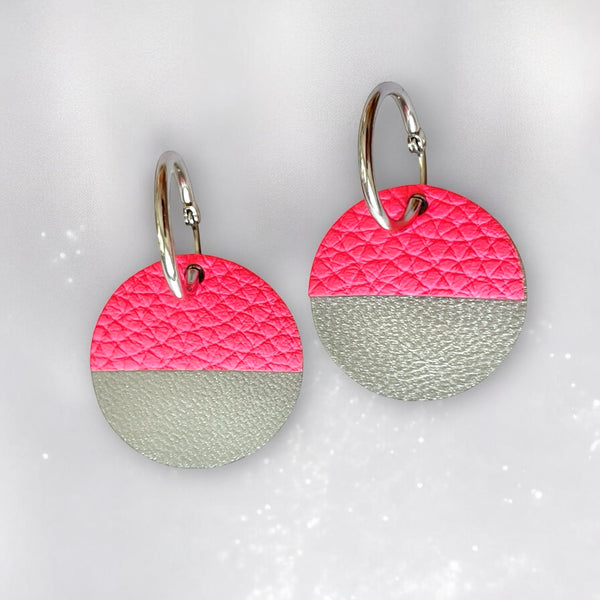 Boucles créoles dorées avec pendentifs en forme de disques et demi-lunes en cuirs rose fluo grainé et gris métallisé, sur fond gris