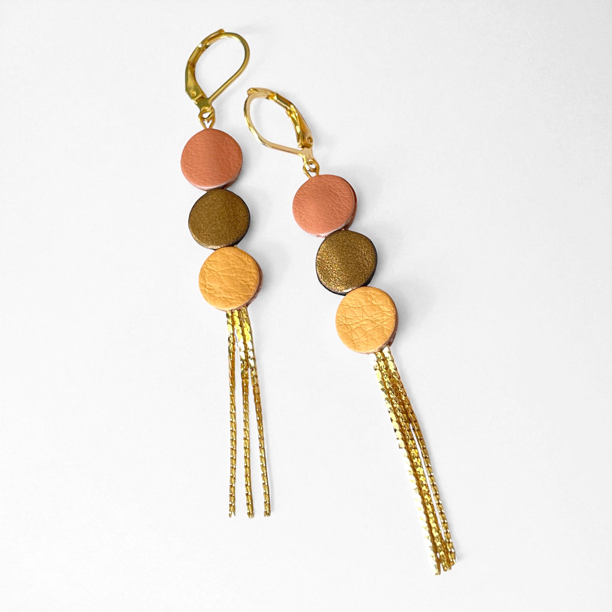Longues et fines boucles d'oreilles Nune à franges dorées avec 3 petits disques de cuir recyclé rose pêche, bronze métallisé et mangue, sur fond blanc. Modèle Janis