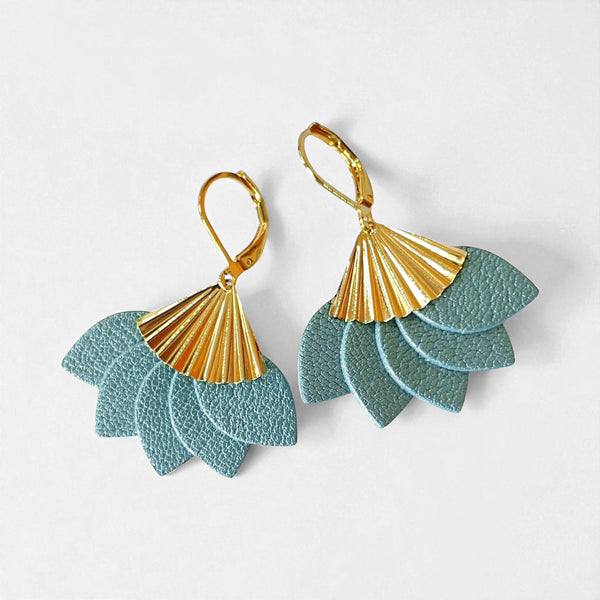 boucles d'oreilles dorées en forme éventail en cuir recyclé bleu gris nacré de la marque Nune modèle Sakura, sur fond de cuir blanc