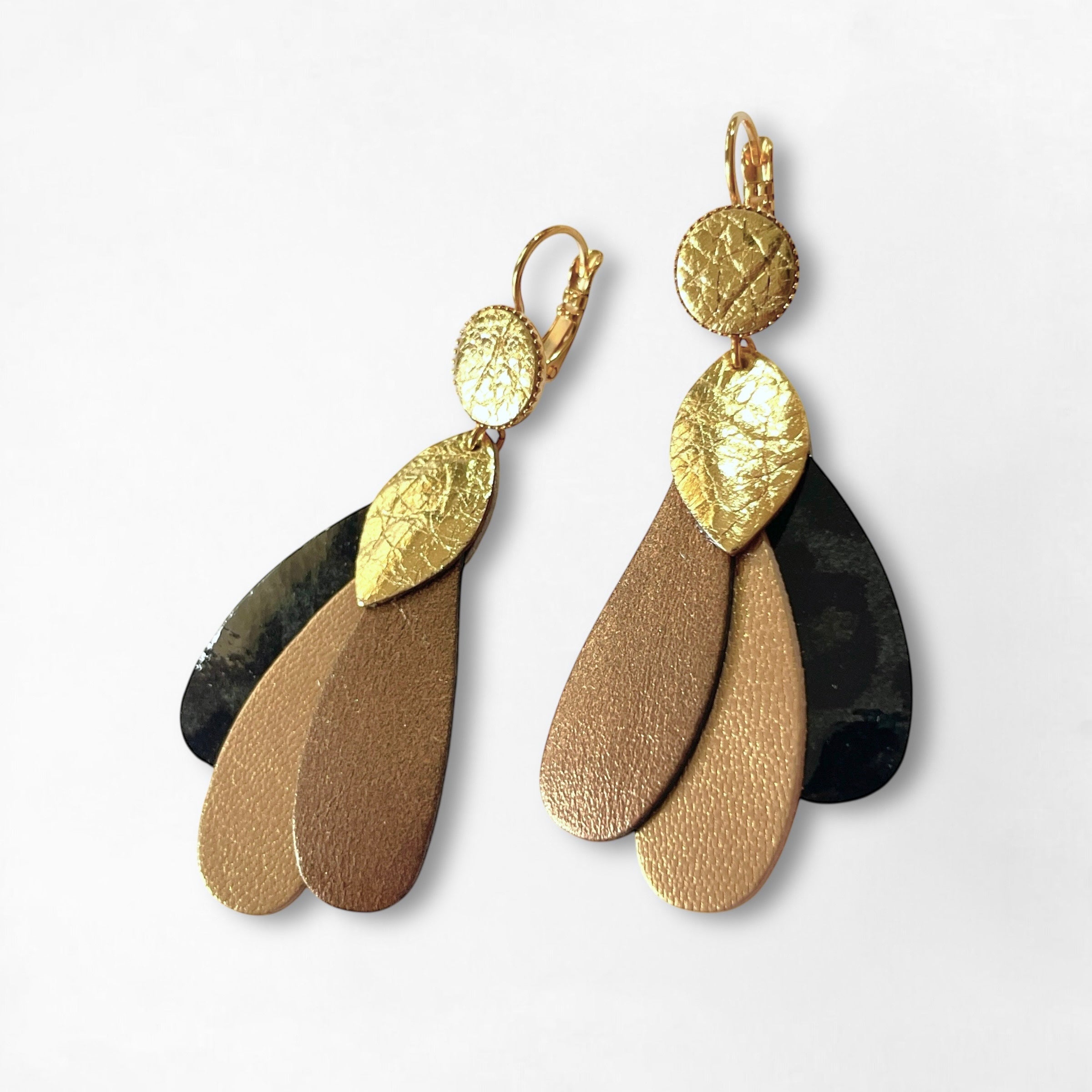 Paire de grandes boucles d'oreilles dorées en forme de plumes de paon, en cuirs recyclés doré clair, bronze métallisé, bronze doré et léopard noir vernis, sur fond blanc. Modèle Paon de Nune.