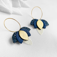 Charger l&#39;image dans la galerie, Créoles dorées en forme de fleurs de Lotus en cuirs bleu nuit grainé métallisé, bleu nuit et doré satiné sur fond blanc
