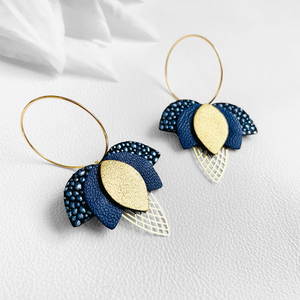 Créoles dorées en forme de fleurs de Lotus en cuirs bleu nuit grainé métallisé, bleu nuit et doré satiné sur fond blanc