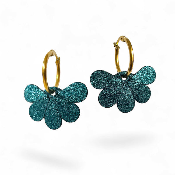 Boucles d'oreilles créoles dorées avec pendentifs en cuir bleu paon pailleté en forme de fleurs, sur fond blanc