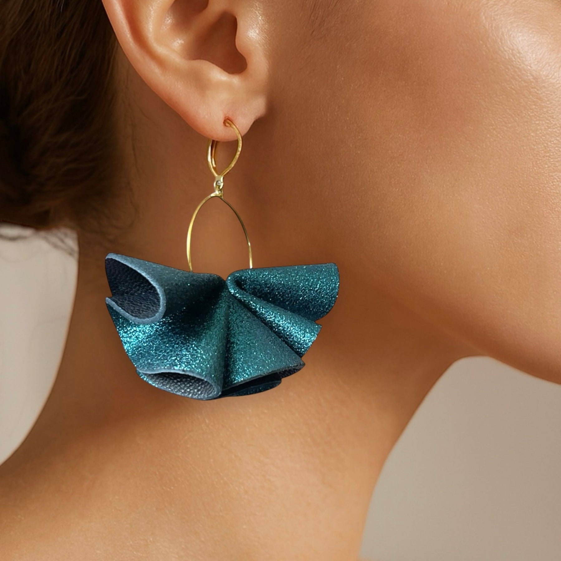 Grandes boucles d'oreilles dorées aériennes et sculpturales en cuir plissé bleu paon pailleté, portées à l'oreille