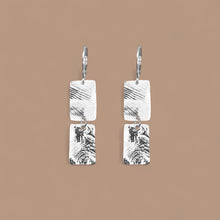 Charger l&#39;image dans la galerie, Boucles d&#39;oreilles pendantes composées de 2 rectangles en métal martelé argentées, sur fond beige
