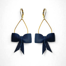 Charger l&#39;image dans la galerie, Boucles d&#39;oreilles dorées pendantes et légères en forme de gouttes, décorées de délicats nœuds de rubans de cuir bleu marine satiné, sur fond blanc. Modèle Séraphine de Nune.
