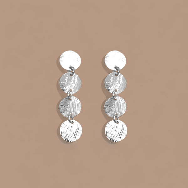 Fines puces d'oreilles pendantes en chapelet de 4 petits sequins ronds en métal martelé argenté, sur fond beige