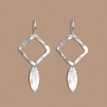 Charger l&#39;image dans la galerie, Boucles d&#39;oreilles argentées avec pendentif en forme de losanges et pointes, sur fond beige
