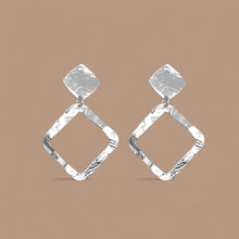 Charger l&#39;image dans la galerie, Boucles d&#39;oreilles puces argentées en métal martelé avec pendentif en forme de losange, sur fond beige
