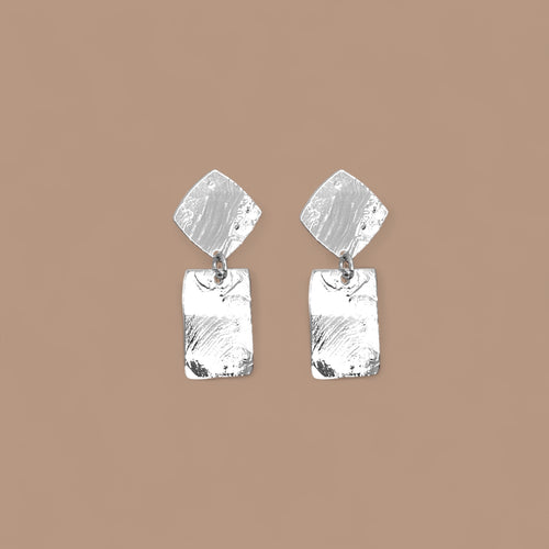 Petites puces d'oreilles losanges avec pendant rectangulaire en métal martelé argenté, sur fond beige