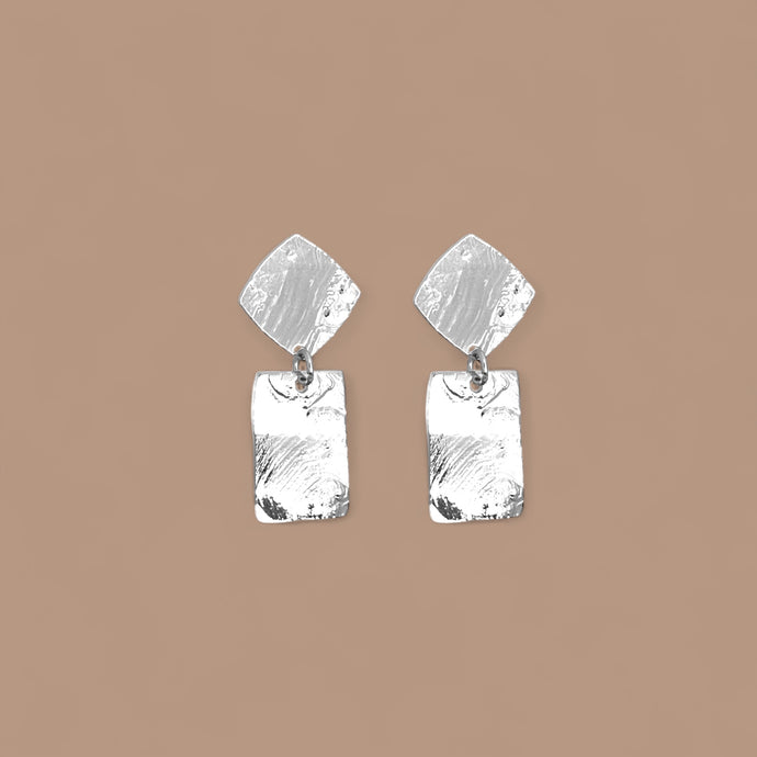 Petites puces d'oreilles losanges avec pendant rectangulaire en métal martelé argenté, sur fond beige