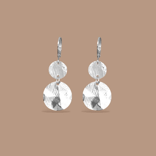 Petites boucles d'oreilles argentées pendantes avec 2 petits sequins ronds en métal martelé, sur fond beige