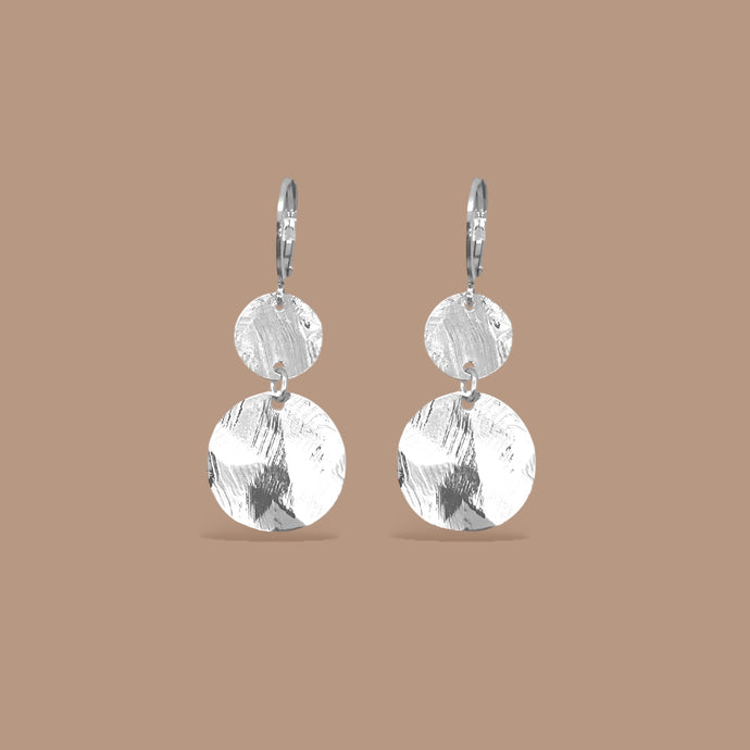 Petites boucles d'oreilles argentées pendantes avec 2 petits sequins ronds en métal martelé, sur fond beige