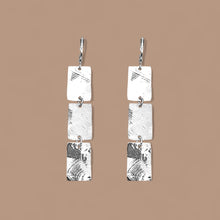 Charger l&#39;image dans la galerie, Boucles d&#39;oreilles pendantes en chapelet de 3 rectangles en métal martelé argenté, sur fond beige
