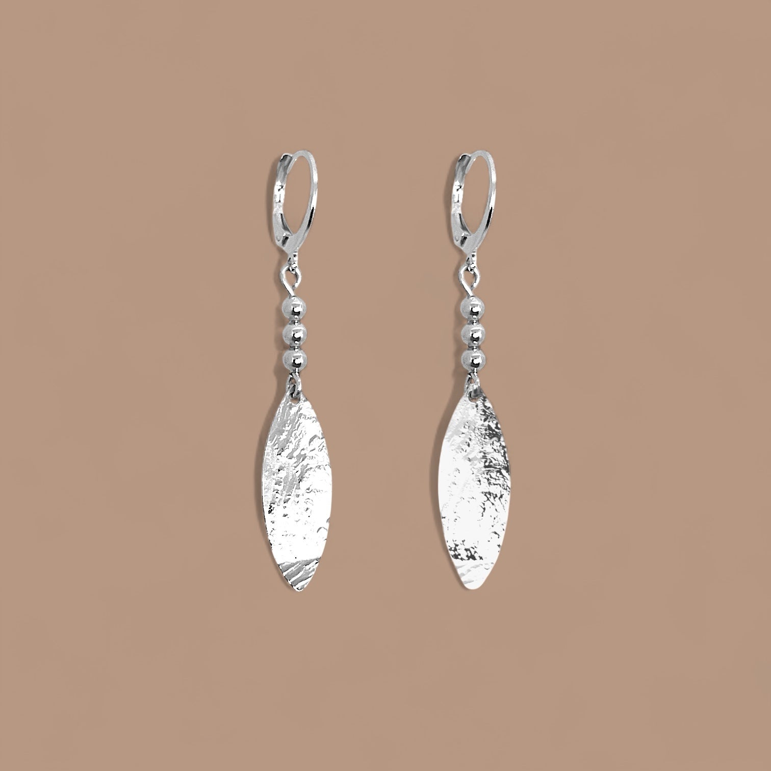 Boucles d'oreilles argentées fines pendantes longues en pointes, sur fond beige