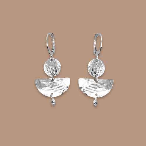 Petites boucles d'oreilles argentées pendantes en forme de demi-lunes, sur fond beige