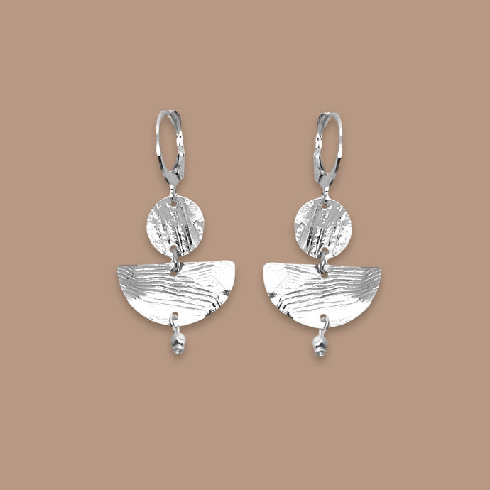 Petites boucles d'oreilles argentées pendantes en forme de demi-lunes, sur fond beige