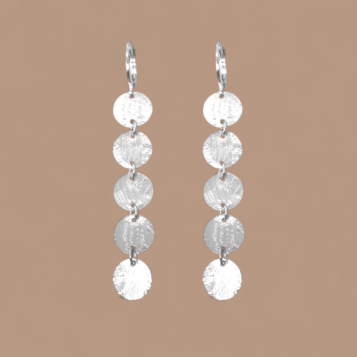 Fines longues boucles d'oreilles argentées pendantes en chapelet de 5 petits sequins ronds, sur fond beige