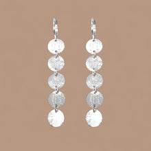 Charger l&#39;image dans la galerie, Fines longues boucles d&#39;oreilles argentées pendantes en chapelet de 5 petits sequins ronds, sur fond beige
