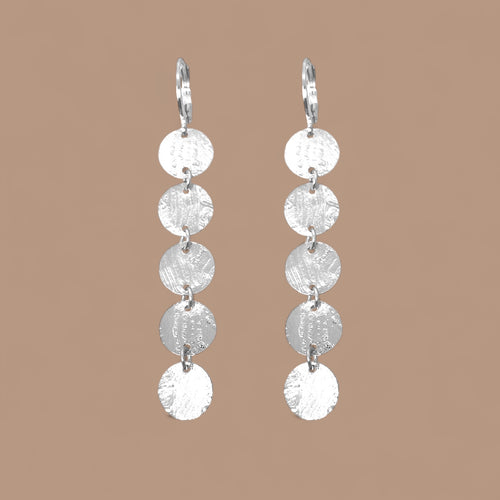 Fines longues boucles d'oreilles argentées pendantes en chapelet de 5 petits sequins ronds, sur fond beige