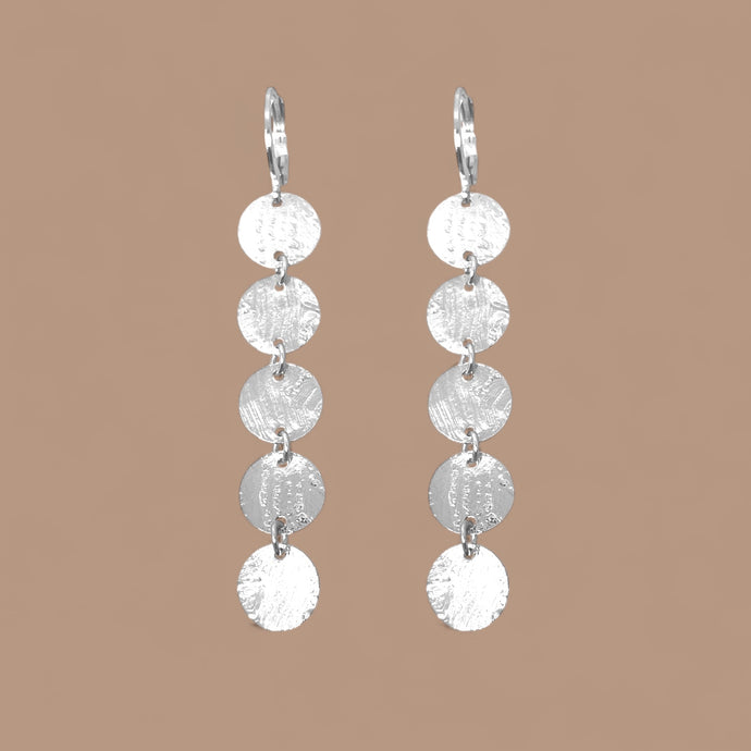 Fines longues boucles d'oreilles argentées pendantes en chapelet de 5 petits sequins ronds, sur fond beige