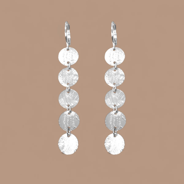 Fines longues boucles d'oreilles argentées pendantes en chapelet de 5 petits sequins ronds, sur fond beige