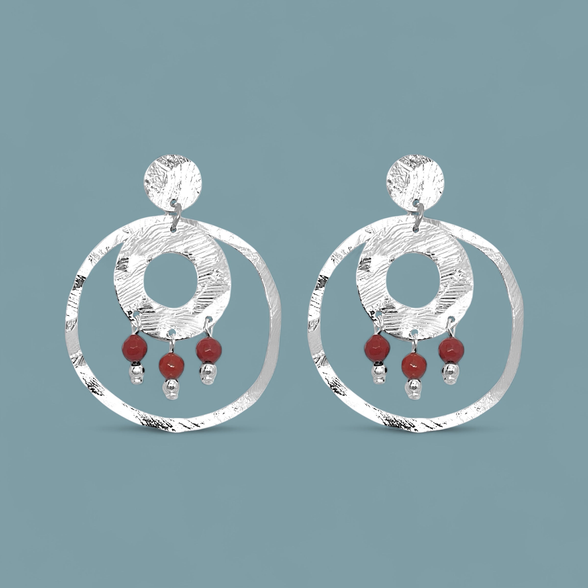 Grandes boucles d'oreilles puces créoles dorées pendantes longues rondes avec double anneau et petites perles en mokaïte acajou, sur fond bleu gris
