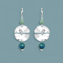 Charger l&#39;image dans la galerie, Boucles d&#39;oreilles pendantes de forme ronde avec 2 demi-lunes, en métal martelé argenté et perles d&#39;amazonite et d&#39;apatite bleue, sur fond bleu gris
