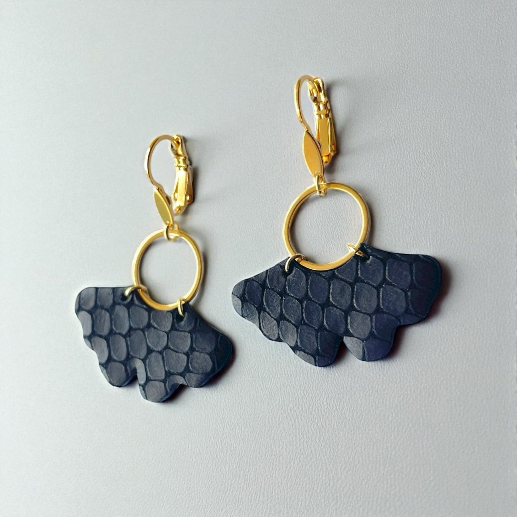 boucles d'oreilles dorées en forme de feuille de gingko en cuir noir mat façon lézard, sur fond blanc