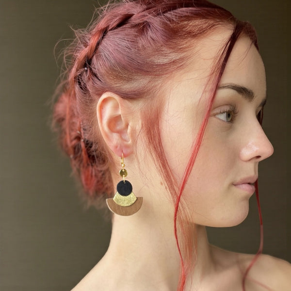 boucle d'oreille dorée Nune modèle Hestia en cuirs beige amande, noir satiné et doré satiné portée par un modèle de profil aux cheveux rouges et au teint pâle