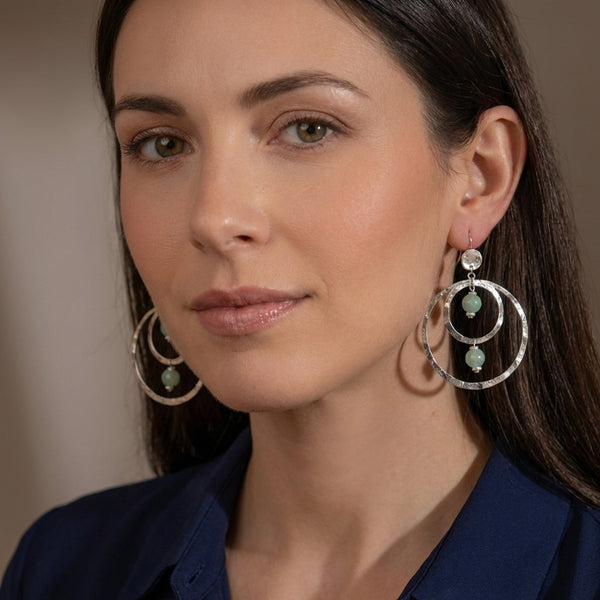 Grandes boucles d'oreilles créoles en métal martelé argenté et perles minérales naturelles d'amazonite, de forme ronde, avec doubles anneaux, portées aux oreilles par une femme brune