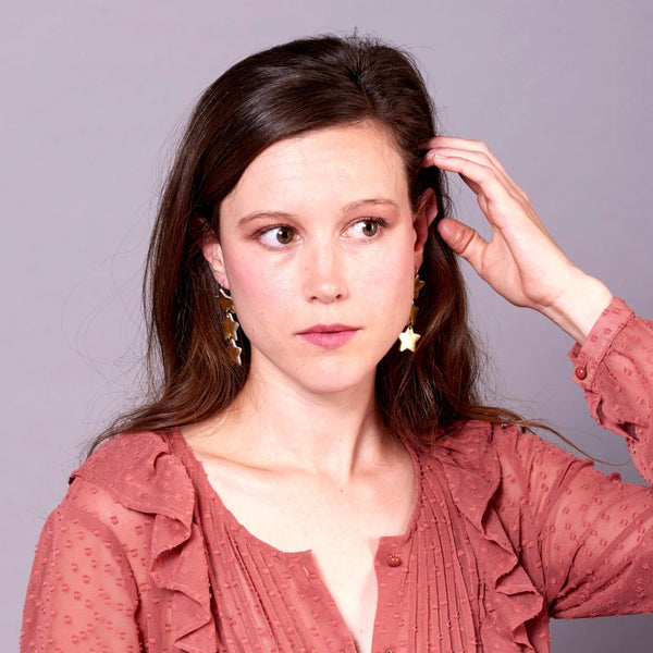 NUNE Boucles d'oreilles Starlight, chapelet d'étoiles en cuir recyclé doré, portées par une jeune femme aux cheveux longs bruns, vue de face