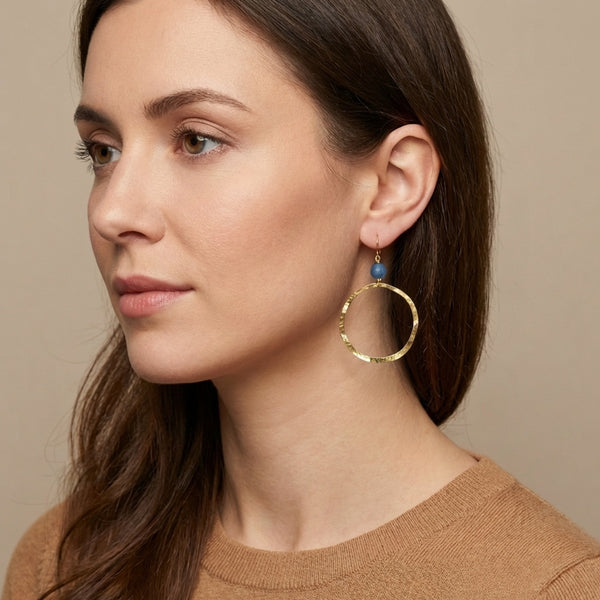 Boucles d'oreilles créoles de forme ronde en métal martelé doré à l'or fin et perles d'aventurine, portées à l'oreille par une femme brune