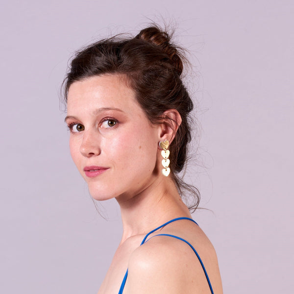 Puce d'oreille Tamaya, chapelet de petits cœurs en cuir doré recyclé, portée par une jeune femme aux cheveux bruns, de côté