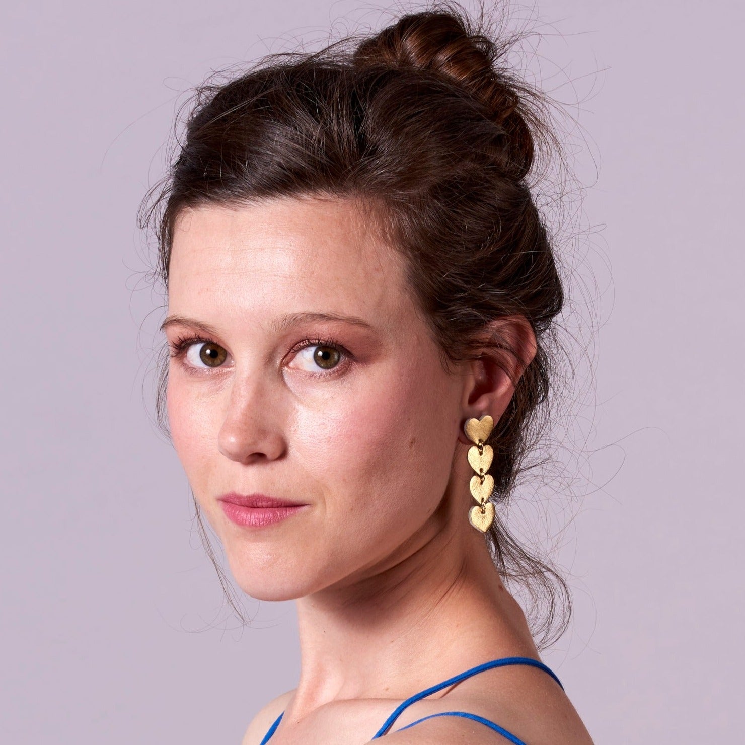 Puce d'oreille Tamaya, chapelet de petits cœurs en cuir doré recyclé, portée par une jeune femme aux cheveux bruns, de profil