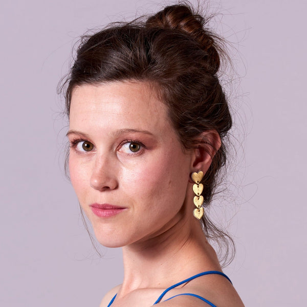 Puce d'oreille Tamaya, chapelet de petits cœurs en cuir doré recyclé, portée par une jeune femme aux cheveux bruns, de profil