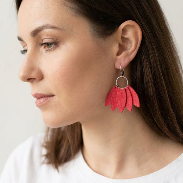 Grandes boucles d'oreilles argentées en forme de couronne de plumes en cuir rose saumon, portées à l'oreille par une femme