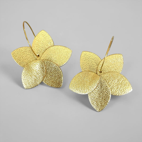 Boucles d'oreilles créoles Tiara en forme de grosse fleur de tiaré en cuir doré satiné et anneaux dorés, sur fond gris