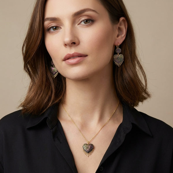 Boucles d'oreilles dorées en forme de cœurs style ex-voto et collier assorti en cuir pailleté recyclé noir pailleté irisé, portés par une femme brune