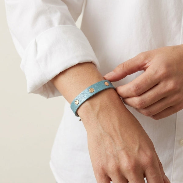 Bracelet argenté en cuirs bicolore bleu gris nacré et or rosé froissé, porté au poignet