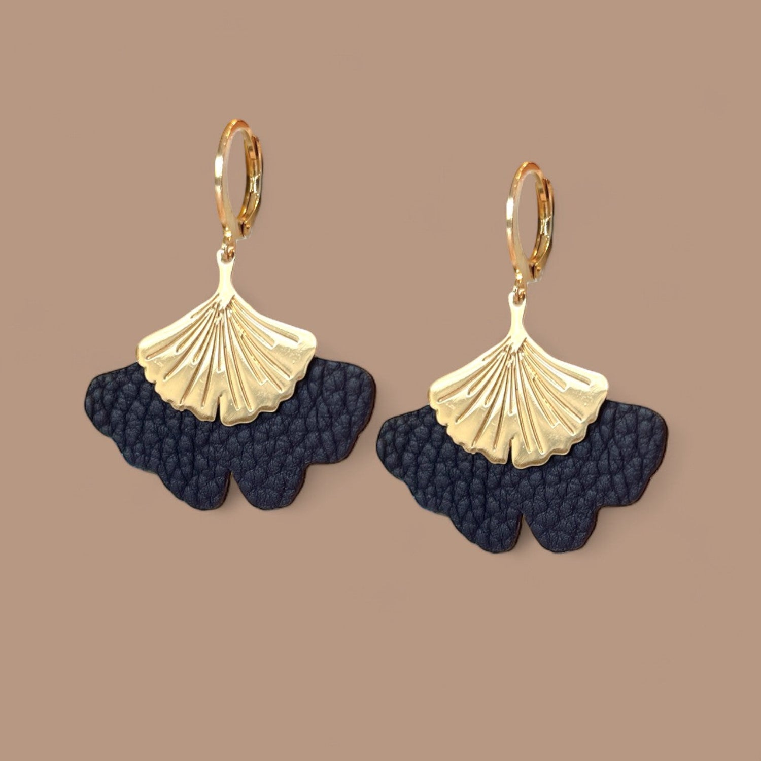 Boucles d'oreilles dorées pendantes en cuir bleu nuit grainé en forme de gingko, sur fond beige