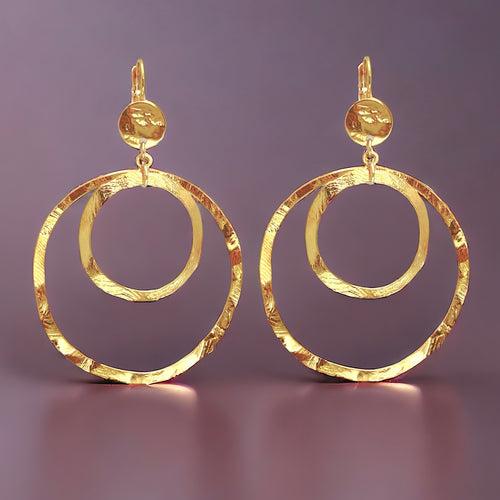 Grandes boucles d'oreilles créoles dorées à double anneau en métal martelé, avec attaches-dormeuses, sur fond violet