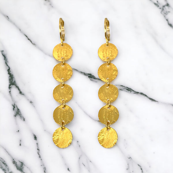 Fines longues boucles d'oreilles dorées pendantes en chapelet de 5 petits sequins ronds, sur fond marbre blanc