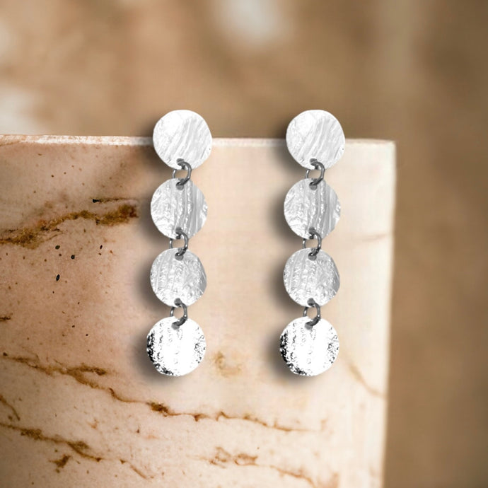 Fines puces d'oreilles pendantes en chapelet de 4 petits sequins ronds en métal martelé argenté, accrochées sur un pot en marbre beige