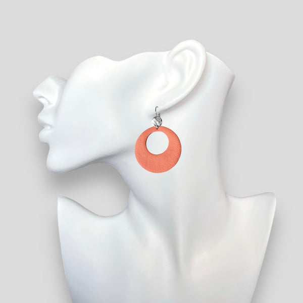 Boucles d'oreilles argentées, grandes créoles rondes en cuir saumon clair au style vintage, portées à l'oreille sur un buste blanc