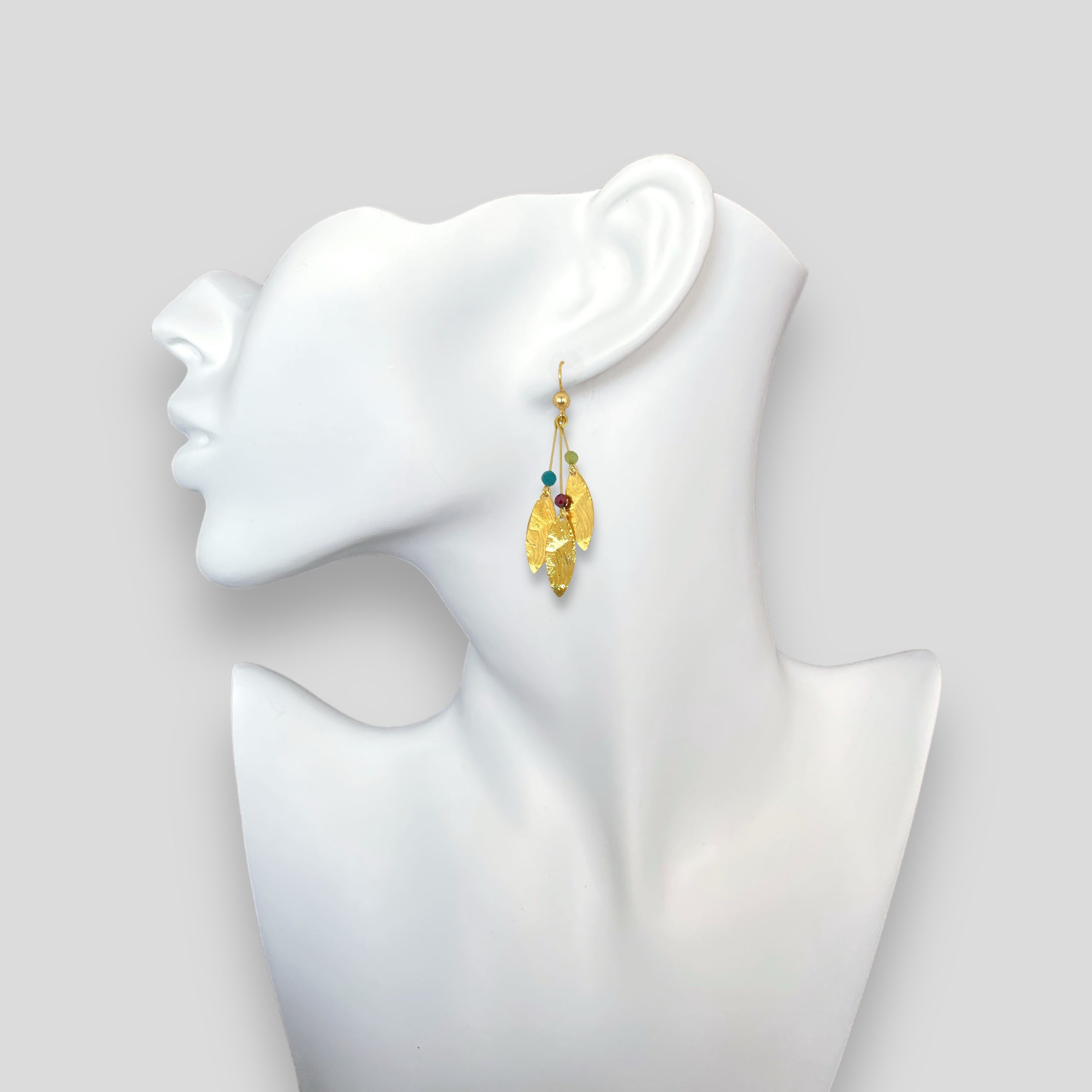 Longues boucles d'oreilles fines avec trois pointes en métal martelé doré à l'or fin et petites perles de pierres naturelles, portées à l'oreille sur fond blanc